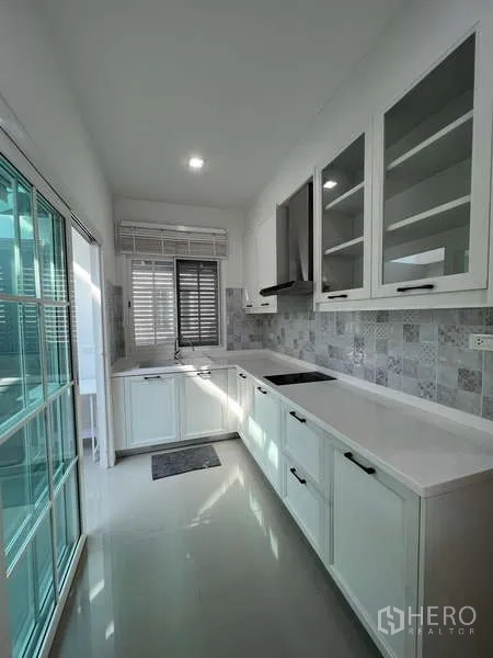 Detached House for rent or sale in Khan Na Yao, Bangkok - Modern galley kitchen with white cabinetry, hob, hood and sliding glass door.