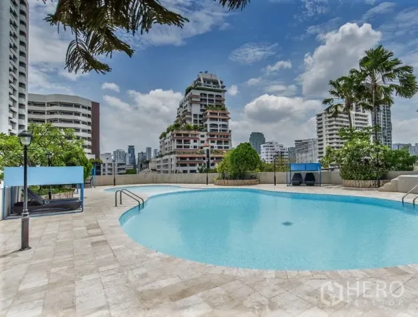 Condominium for rent in Watthana, Bangkok - Outdoor swimming pool deck with city skyline views and tropical greenery at the condominium.