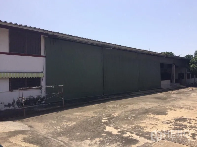 Warehouse for rent in Samut Prakan - Long warehouse facade with large sliding doors beside an open concrete yard.