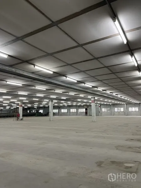 Factory for rent in Phra Samut Chedi, Samut Prakan - Vast factory interior with grid ceiling, bright fluorescent lighting and open concrete floor.