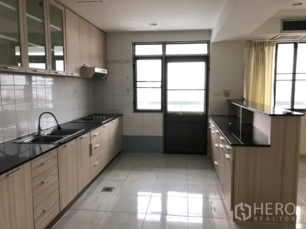 Condominium for rent in Watthana, Bangkok - Spacious kitchen with light wood cabinets, black countertops and large windows.