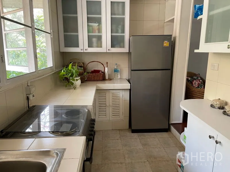 Condominium for rent in Watthana, Bangkok - Bright closed kitchen with large windows, glass-front cabinets, stove and stainless refrigerator.