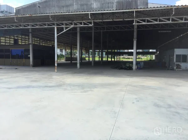 Warehouse for rent in Khlong Luang, Pathum Thani - Open warehouse interior in Khlong Luang with high steel truss roof, concrete floor, and a large covered loading area.