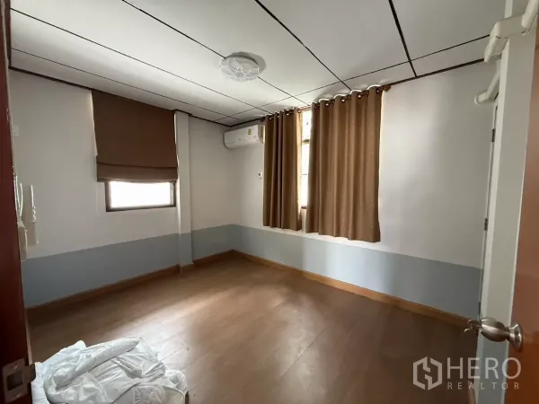 Detached House for rent in Phra Khanong, Bangkok - Bright bedroom with wood floors, air conditioner and two curtained windows.