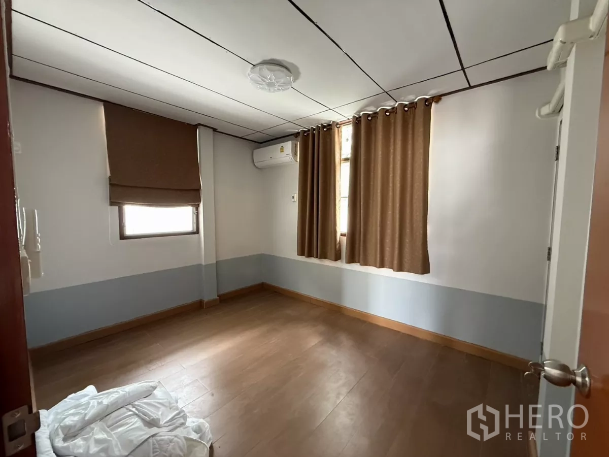 Detached House for rent in Phra Khanong, Bangkok - Bright bedroom with wood floors, air conditioner and two curtained windows.