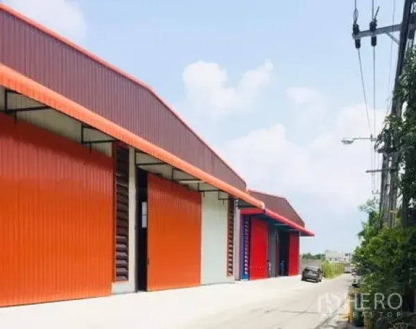 Warehouse for rent in Khan Na Yao, Bangkok - Row of modern orange steel warehouses with large roller doors along a quiet road in Khan Na Yao, Bangkok.