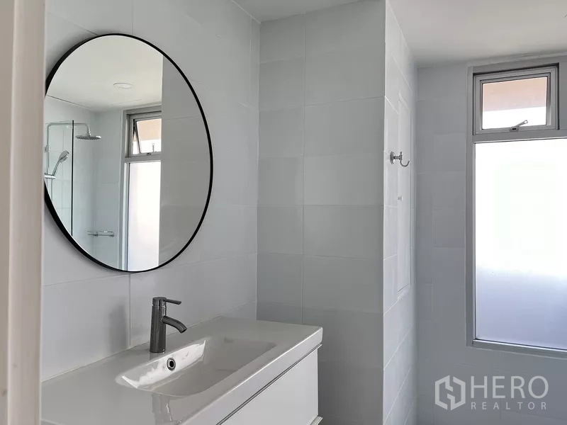 Condominium for rent in Khlong Toei, Bangkok - Modern bathroom vanity with round mirror, sleek faucet and natural light from the window.