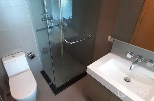 Condominium for rent in Khlong Toei, Bangkok - Bathroom with glass-enclosed shower, modern vanity and toilet.