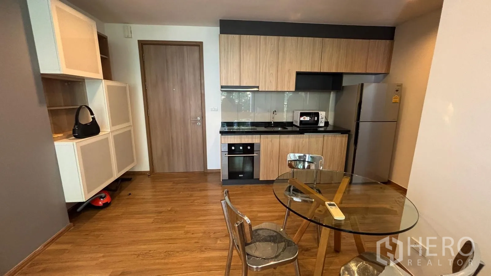 公寓 for rent or sale in Watthana, Bangkok - 开放式厨房配木质橱柜、黑色台面、烤箱、微波炉、冰箱及圆形玻璃餐桌。