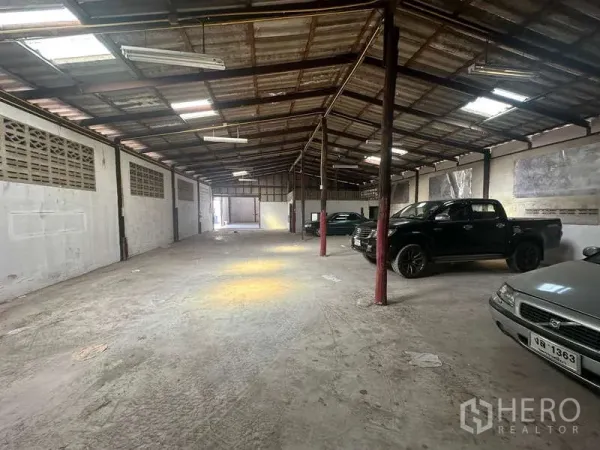 Warehouse for rent in Suan Luang, Bangkok - Spacious open-plan warehouse interior with concrete floor, steel roof and vehicles parked along the side.
