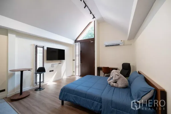 Detached House for rent in Phra Khanong, Bangkok - Bright bedroom with high ceiling, wall-mounted TV, desk and air conditioner.