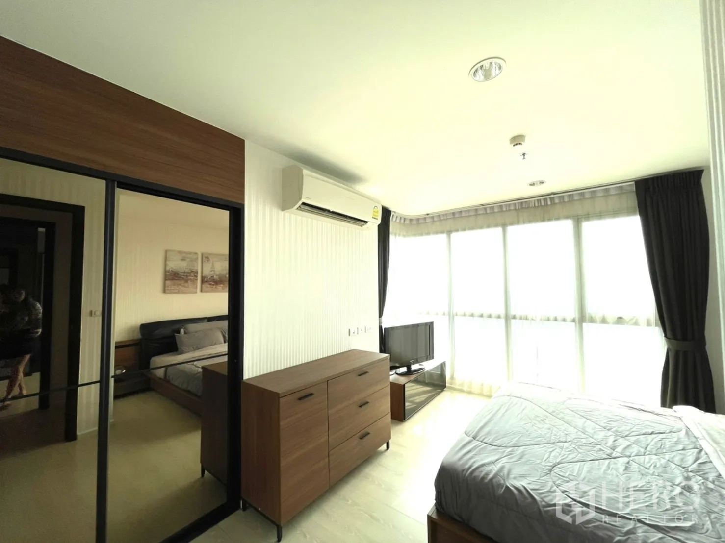 Condominium for sale in Sathon, Bangkok - Corner master bedroom with floor-to-ceiling windows, dresser, TV stand and air conditioner.