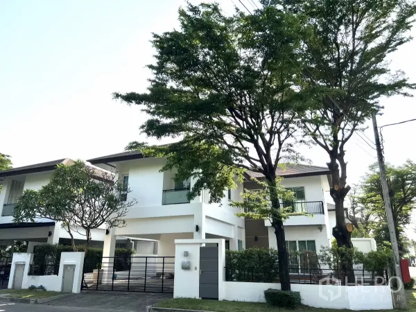 独立式住宅 出租或出售在Saphan Sung, Bangkok - 两层现代白色独栋屋，带阳台、行道树与铁栅大门，街景安静。