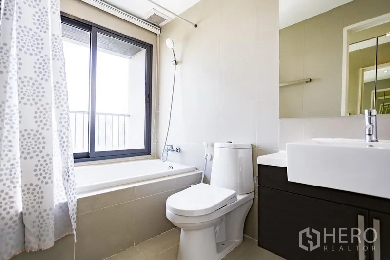 Condominium for rent in Khlong Toei, Bangkok - Clean bathroom with bathtub-shower combo, window, vanity sink and toilet.