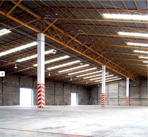 Factory for rent in Samut Prakan - Expansive warehouse interior with high steel truss roof, skylights, concrete floor, and multiple loading bays.