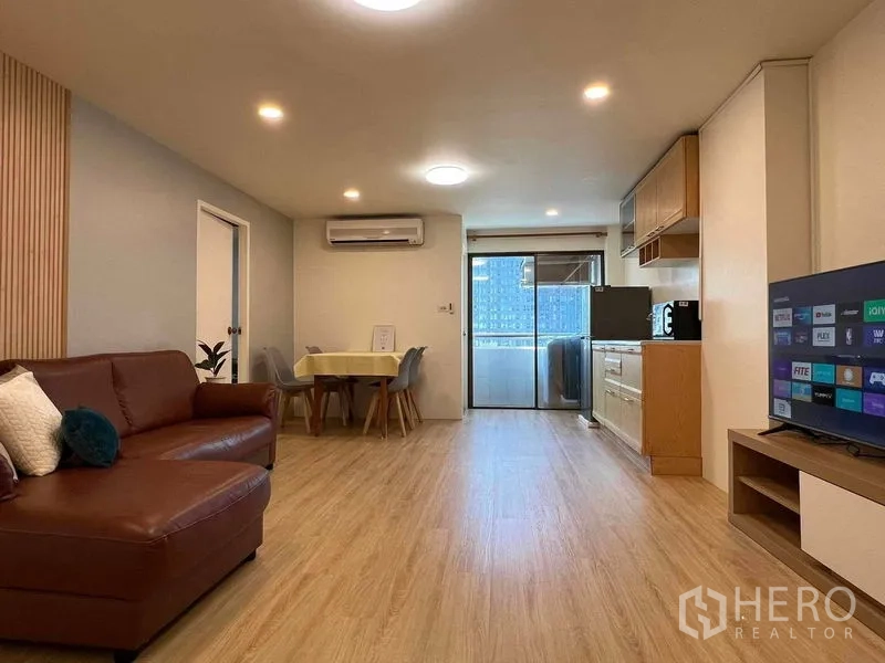 公寓 出租在Ratchathewi, Bangkok - 开放式客厅连厨房和餐桌，玻璃门通阳台，可见城市建筑。