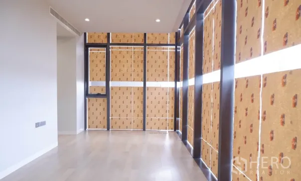 Condominium for sale in Watthana, Bangkok - Spacious living area with light wood floors and floor-to-ceiling windows wrapped for protection.