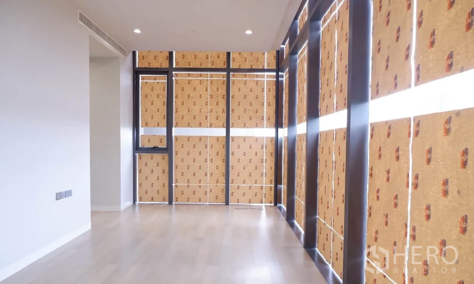 Condominium for sale in Watthana, Bangkok - Spacious living area with light wood floors and floor-to-ceiling windows wrapped for protection.