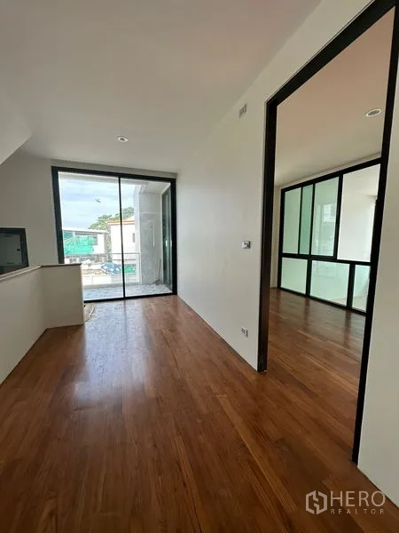 Detached House for rent in Watthana, Bangkok - Hallway with sliding glass doors to a balcony and an adjacent room with a glass partition wall.
