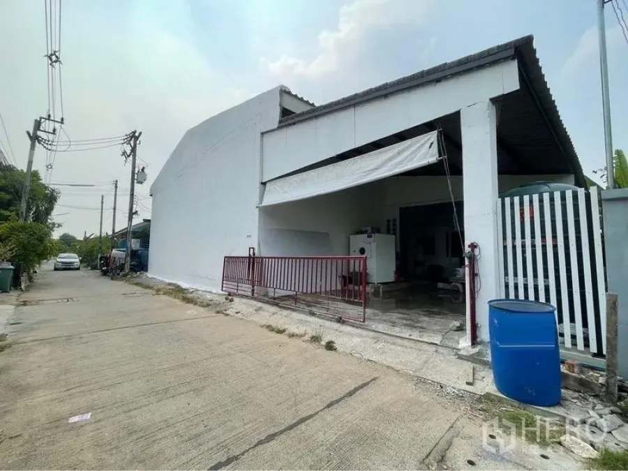 Warehouse for sale in Lam Luk Ka, Pathum Thani - Front loading bay with sliding gate and covered entrance facing a quiet local road.