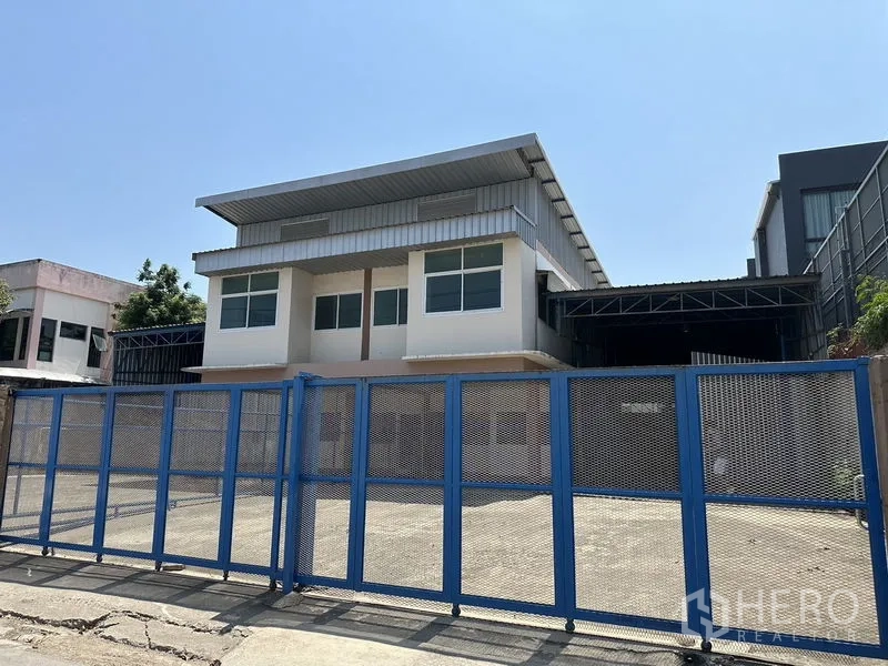 Warehouse for rent in Bueng Kum, Bangkok - Two-storey office-fronted warehouse in Bueng Kum with blue steel gate and wide concrete yard.