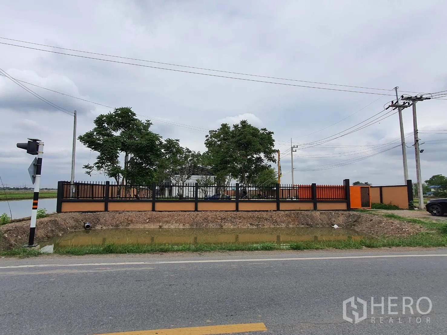 โกดัง for sale in Lam Luk Ka, Pathum Thani - มุมมองจากถนน เห็นรั้วรอบและประตูหน้าโครงการติดถนนสาธารณะ