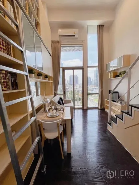 Condominium for rent or sale in Khlong Toei, Bangkok - Loft-style living and dining area with floor-to-ceiling windows, dark wood floors, and a tall built-in bookshelf overlooking a city view.