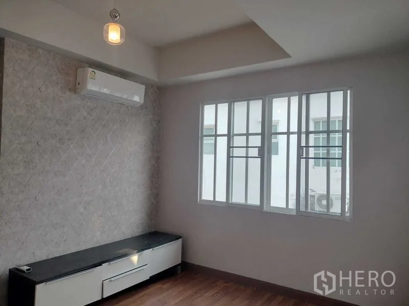 Townhouse for rent in Bueng Kum, Bangkok - Bright room with air conditioner, textured feature wall and low TV console under a window.