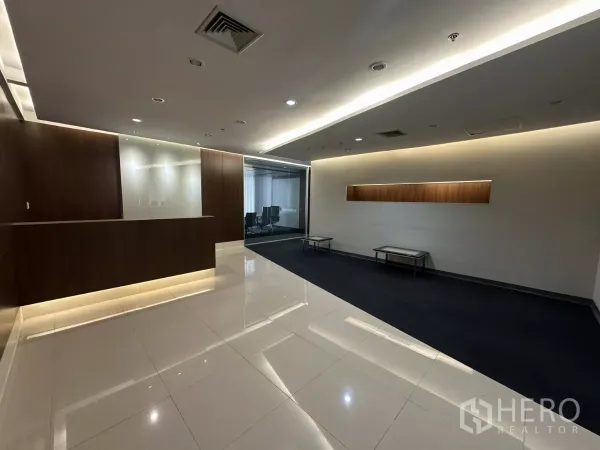 Office Space for rent in Watthana, Bangkok - Reception area with wood feature wall, built-in counter, glossy tile floor and cove lighting, with a glass meeting room beyond.