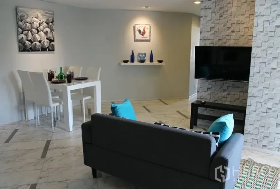 公寓 出租或出售在Watthana, Bangkok - 瓦他那公寓的开放式客餐厅，石材电视墙、壁挂电视与白色餐桌。