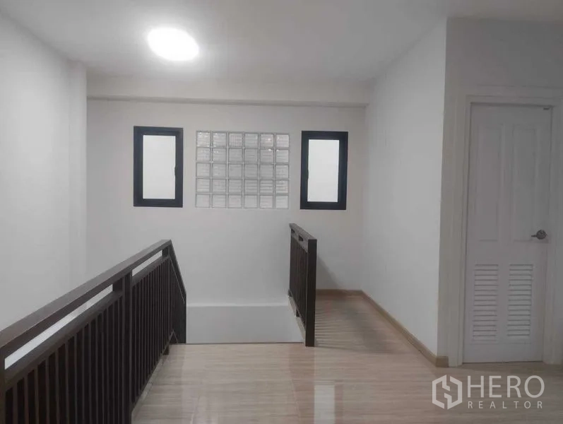 Detached House for sale in Phra Khanong, Bangkok - Upper corridor with railing, ceiling light and a louvered door.