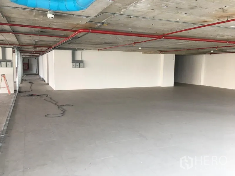 Retail Space for rent in Khlong Toei, Bangkok - Open-plan retail unit with grey tiled floor, white walls, and exposed concrete ceiling with red fire pipes and blue ducting.
