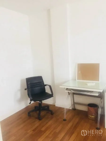 Townhouse for rent in Bang Kapi, Bangkok - Bright study corner with white walls, glass desk and black office chair on wood floor.