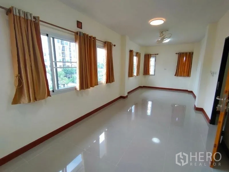 Detached House for rent in Khlong Toei, Bangkok - Bright empty room with glossy tiles and several windows dressed with mustard curtains.