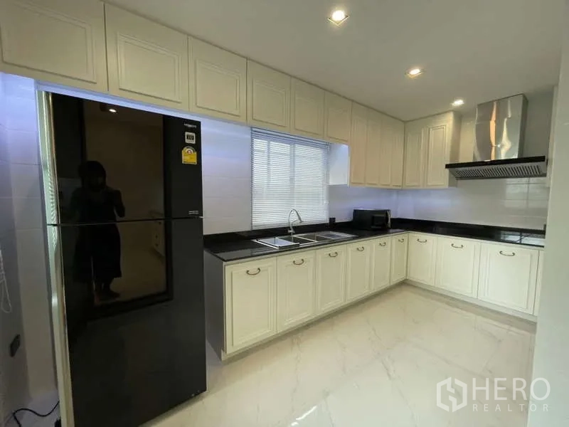 Detached House for rent or sale in Lat Krabang, Bangkok - Bright L-shaped kitchen with white cabinetry, black countertops and a stainless hood.