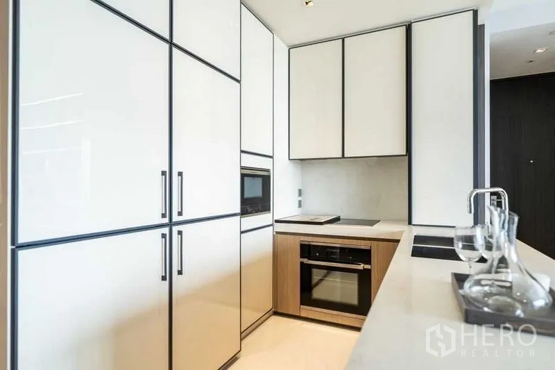 Condominium for rent in Khlong Toei, Bangkok - Sleek U-shaped kitchen with white cabinetry, built-in oven and microwave, and induction cooktop.