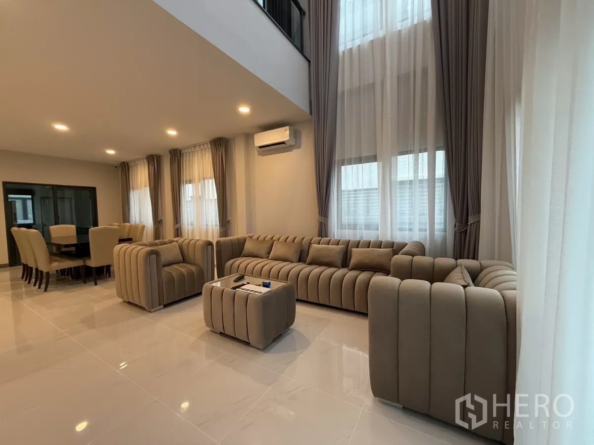 独立式住宅 出租在Bang Phli, Samut Prakan - 开放式客餐厅，米色沙发、挑高天花与落地纱帘。