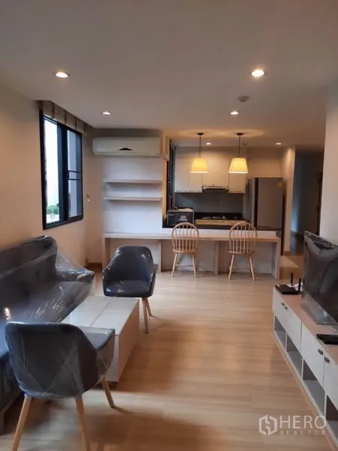 Condominium for rent in Watthana, Bangkok - Open-plan living room with light wood floors, sofa set, TV console and a kitchen island with pendant lights.