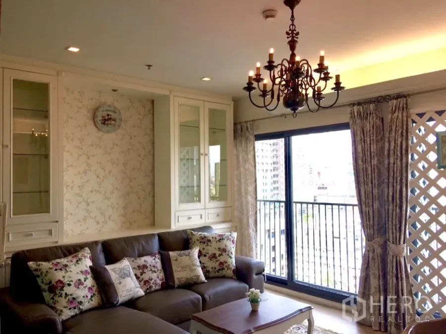 Condominium for rent in Khlong Toei, Bangkok - Bright lounge opening to a balcony with city view, ornate chandelier, large sliding glass doors and classic built-in cabinetry.