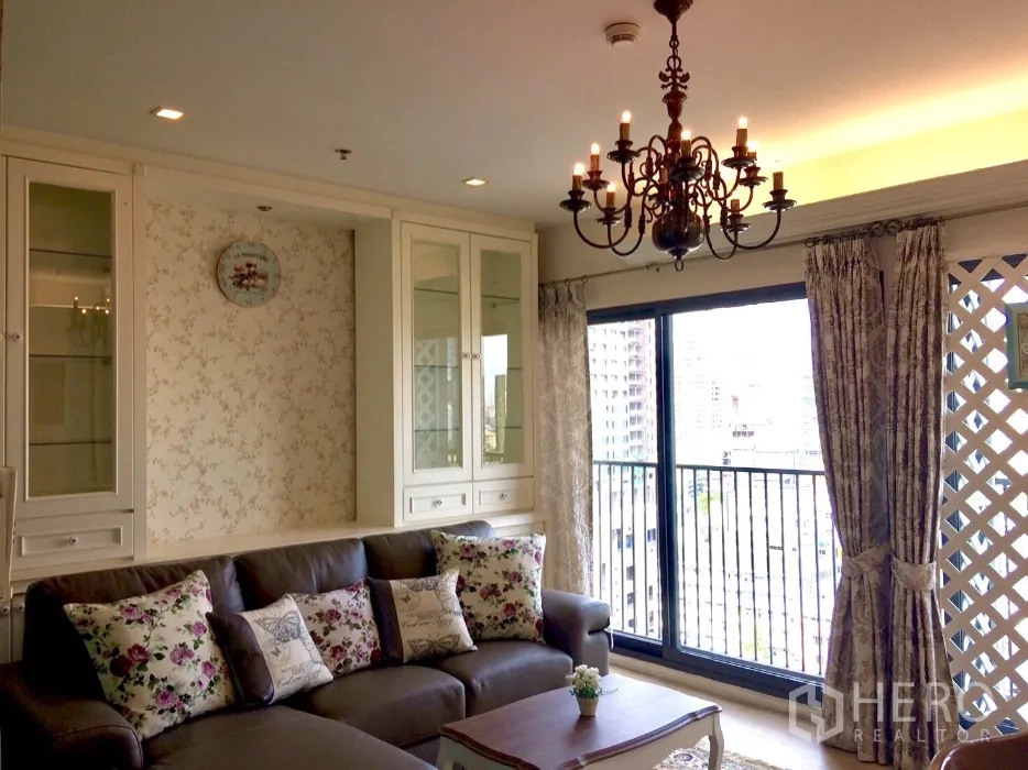 Condominium for rent in Khlong Toei, Bangkok - Bright lounge opening to a balcony with city view, ornate chandelier, large sliding glass doors and classic built-in cabinetry.