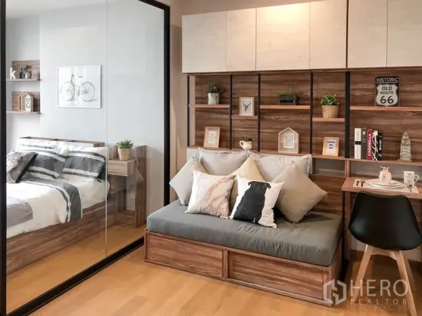 Condominium for rent in Bang Rak, Bangkok - Cozy living area with wooden shelving, sofa daybed, and a glass partition to the bedroom.
