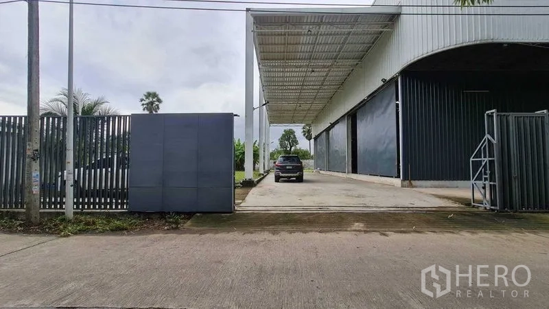 Warehouse for rent in Mueang Nonthaburi, Nonthaburi - Front gate view of the warehouse with wide sliding gates and a long concrete access ramp.