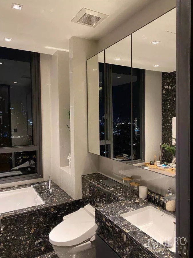 Condominium for rent or sale in Khlong Toei, Bangkok - Bathroom vanity with large mirror, stone countertop and toilet, city lights visible outside.