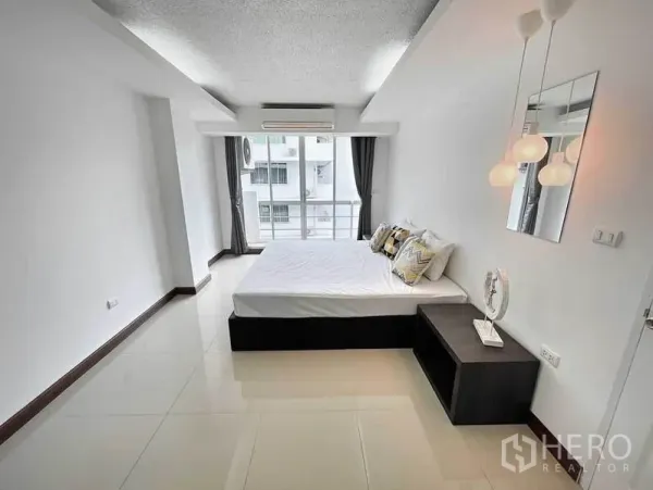 Condominium for rent in Khlong Toei, Bangkok - Spacious master bedroom with bed, pendant lights and sliding glass doors to a balcony.
