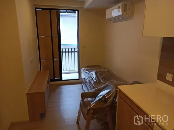 Condominium for sale in Din Daeng, Bangkok - Living area with air conditioner and a sliding door opening to a small balcony.
