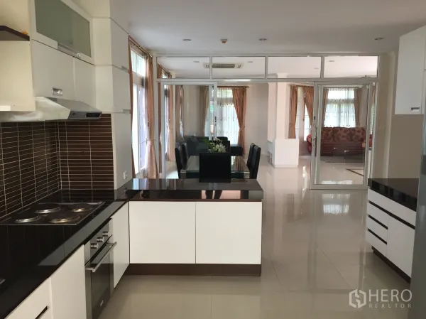 Detached House for rent or sale in Lat Phrao, Bangkok - Modern open kitchen facing dining and living areas with glossy countertops and ample storage.