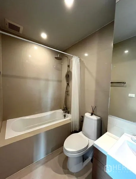 Condominium for rent in Bangkok - Modern bathroom with bathtub, shower over tub, vanity and toilet in neutral tones.