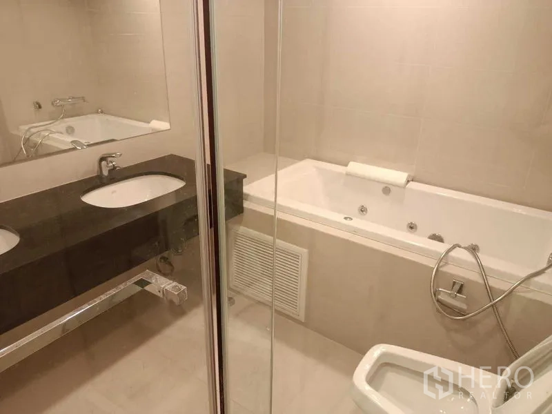 คอนโด ให้เช่าหรือขายในHuai Khwang, Bangkok - ห้องน้ำพร้อมอ่างอาบน้ำจากุซซี ฉากกั้นอาบน้ำกระจก และเคาน์เตอร์ซิงก์ยาว.