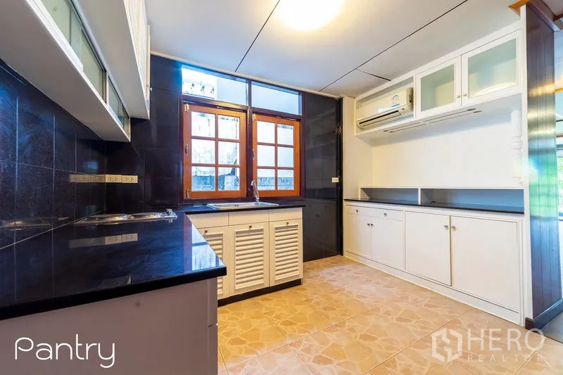 Detached House for rent in Huai Khwang, Bangkok - Bright pantry kitchen with white cabinets, black countertops and tiled floor.