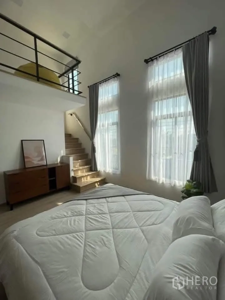 Townhouse for rent in Bang Phli, Samut Prakan - Spacious bedroom with a loft mezzanine and two tall windows with curtains.